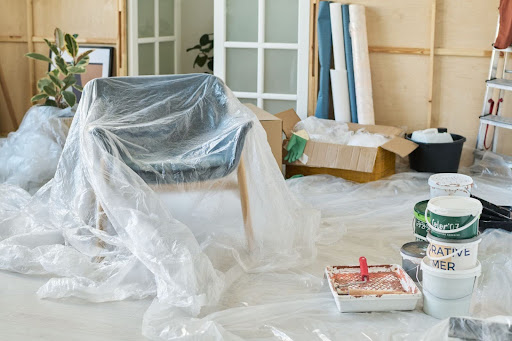 Living room prepared for interior painting with chair and tools covered in plastic sheets