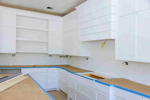 Oil vs Water-Based Cabinet Paint: Which Is Better for Kitchen Cabinets? Kitchen cabinet prep with taped counters during Oil vs Water-Based Cabinet Paint refinishing process.