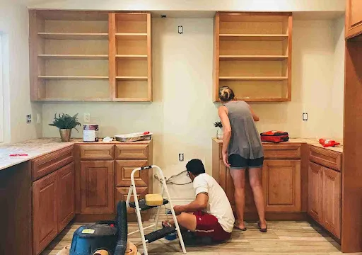 Oil vs Water-Based Cabinet Paint: Which Is Better for Kitchen Cabinets? Homeowners refinishing wood cabinets illustrating Oil vs Water-Based Cabinet Paint application stages.